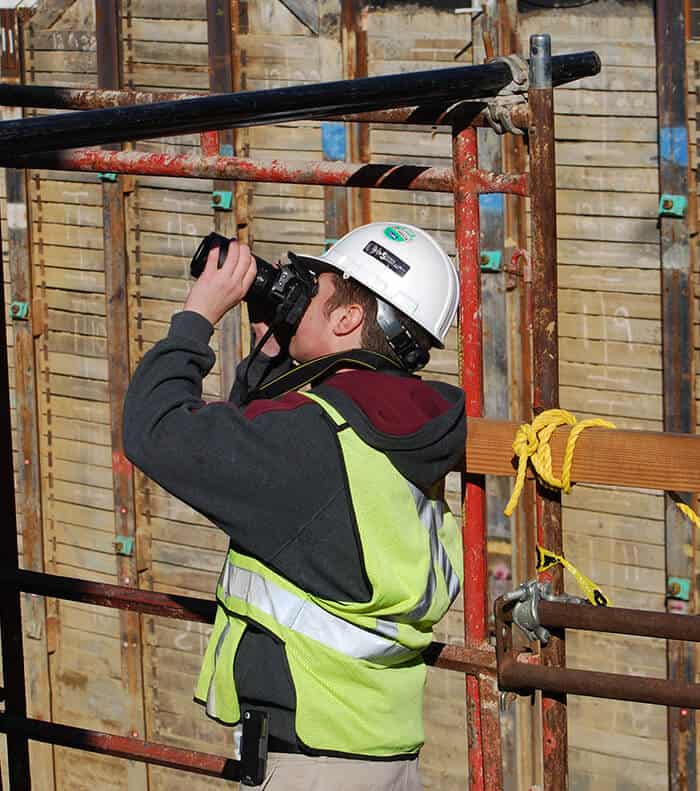 A Seismic Surveys technician is on a scaffold taking photographs for a pre-construction survey.