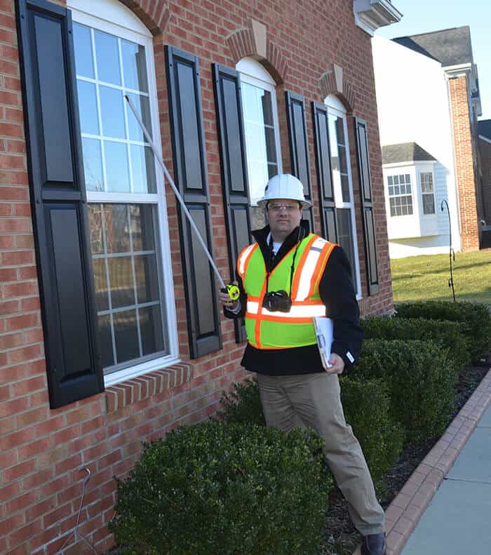 A Seismic Surveys technician with measuring tape outside of a building during a pre-construction survey.