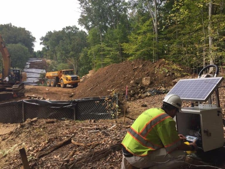 Technician adjusting a solar-powered environmental noise monitoring station at an active mining site