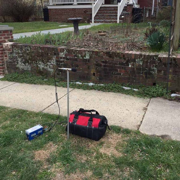 Construction noise monitoring microphone on a residential lawn to track decibel impacts from nearby work